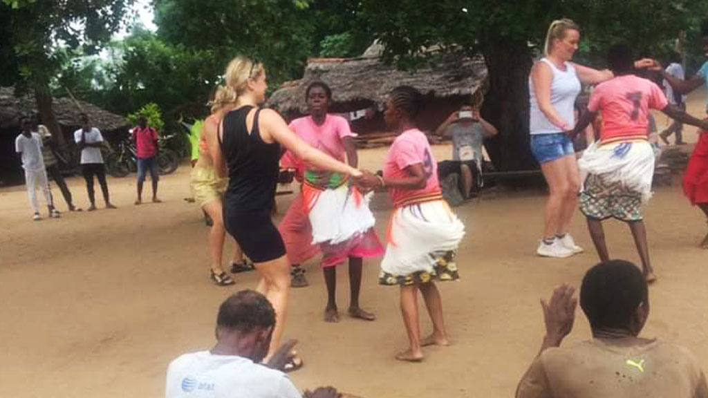 two white women dance with indigenous women in an African village