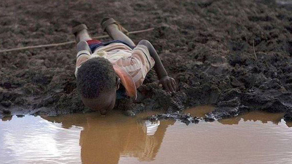 child drinks water from a river lying on the ground