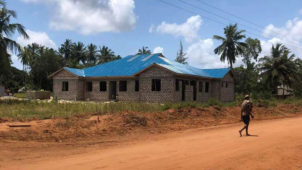 the structure of an orphanage along a dirt road crossed by a barefoot man